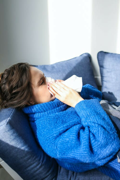 Sick person on a couch blowing their nose into a tissue.